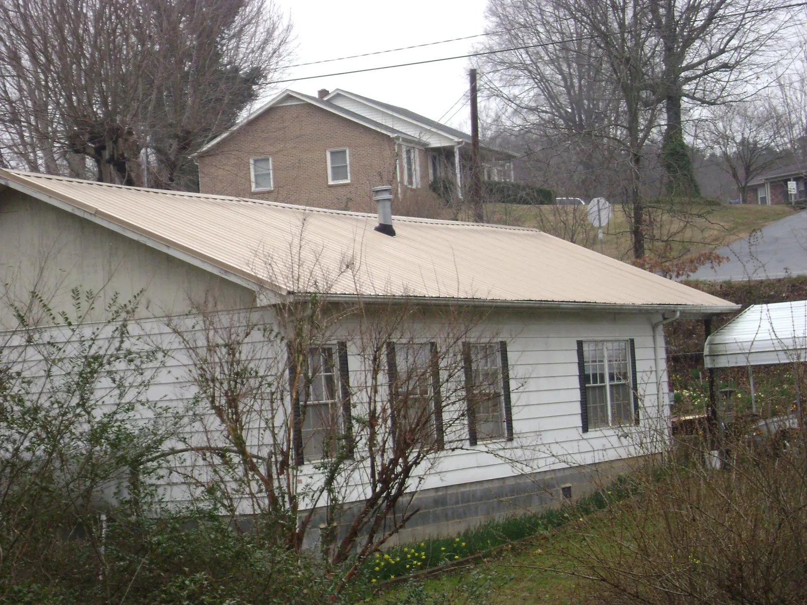 Tan metal roof on a white sided house set into a hillside — Commercial Roofing by Roofing Brothers in Glen
